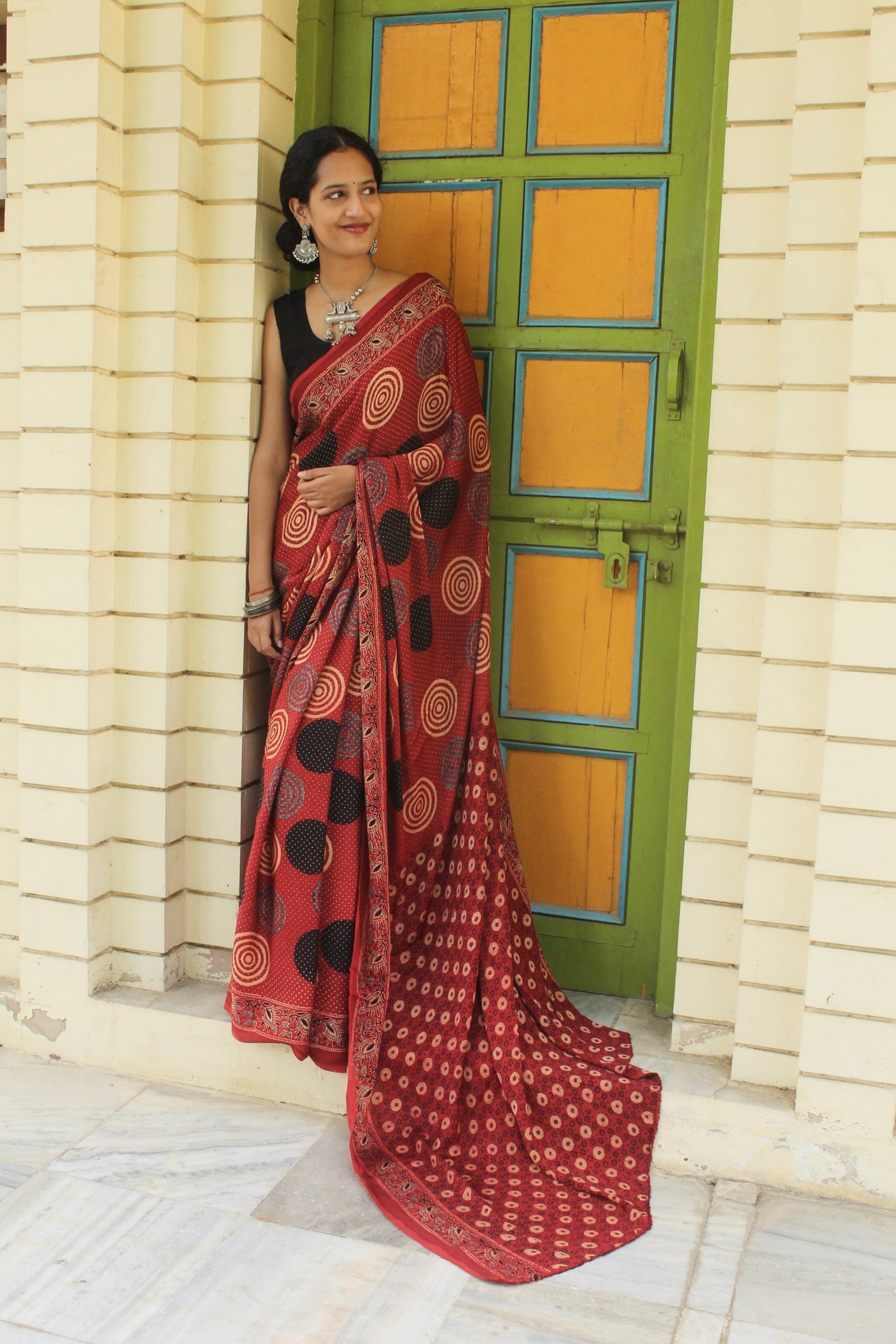 Brick red Ajrakh modal silk saree featuring intricate hand block printed motifs and a graceful drape