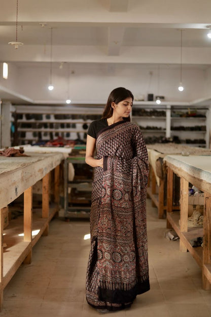 Traditional charcoal black Ajrakh modal silk saree with rich artisanal prints and a soft flowing texture
